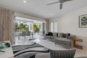 A modern living room with a sofa, a dining area with chairs, and a view of palm trees outside.