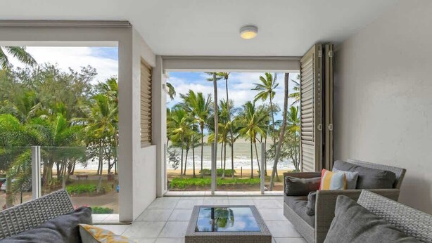 Een moderne woonkamer met een grote glazen deur die leidt naar een balkon met uitzicht op palmbomen en het strand.