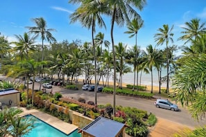 Un resort con piscina, palme, spiaggia e una strada con auto parcheggiate.