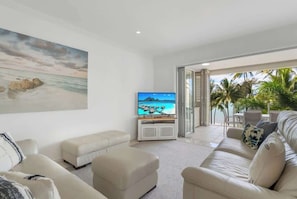 Un soggiorno con televisore, un quadro di grandi dimensioni e vista sulla spiaggia attraverso una porta in vetro.