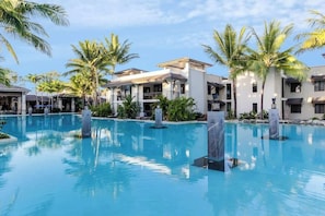 Een resort met een groot zwembad, palmbomen en moderne gebouwen.