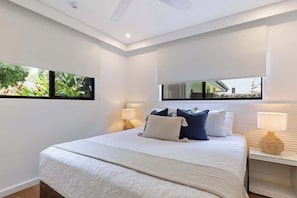 Een moderne slaapkamer met een groot bed, twee bedlampen, een groot raam met uitzicht, en drie ingelijste foto’s aan de muur.