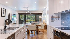 Une cuisine moderne avec des meubles blancs, un coin repas comprenant une table et des chaises, et une vue sur la verdure à l’extérieur.