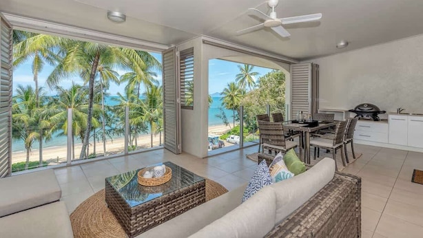 A modern living room with a large glass door leading to a balcony with a beach view. - Opal Dreams—Your Gateway to Beachfront Bliss (Palm Cove)