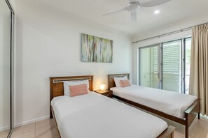 A hotel room with two beds, a ceiling fan, a large window with blinds, and a wall-mounted abstract painting. - Opal Dreams—Your Gateway to Beachfront Bliss (Palm Cove)
