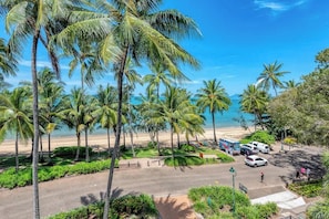 Una vista sulla spiaggia con palme, un'area parcheggio e un cielo azzurro intenso.