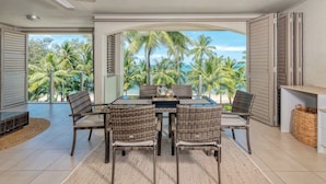 A dining area with a table and chairs, a ceiling fan, and a view of palm trees and the ocean. - Opal Dreams—Your Gateway to Beachfront Bliss (Palm Cove)
