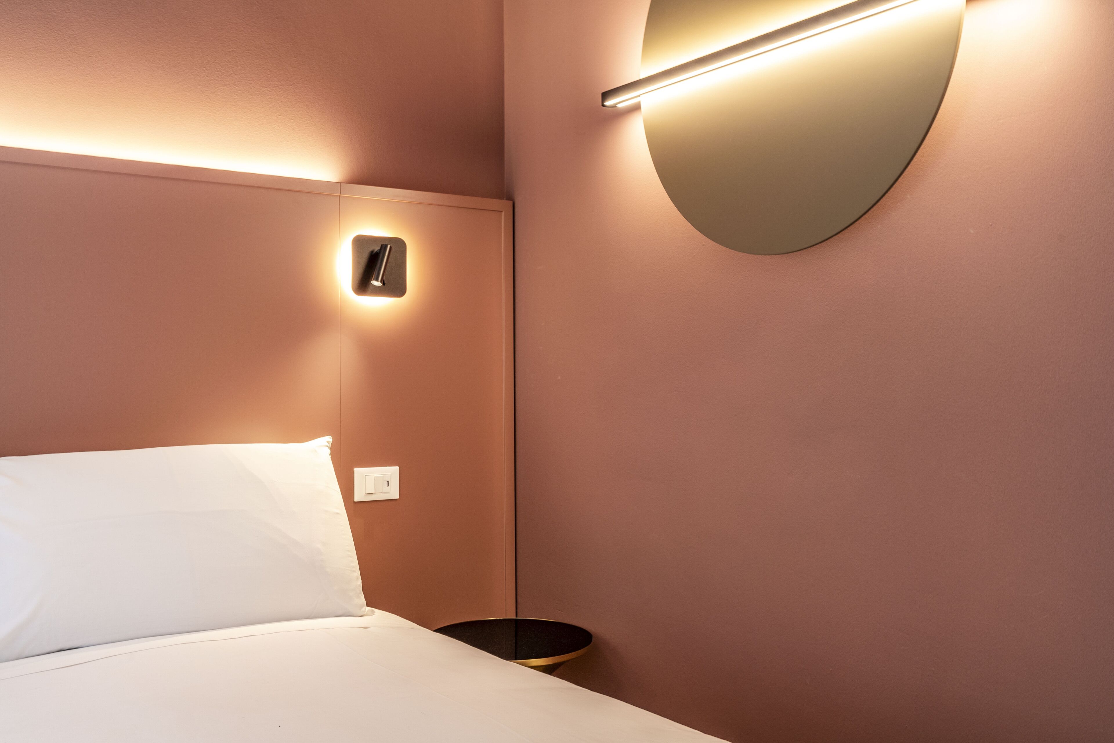 Une chambre d’hôtel avec un lit, une table de chevet, une lampe fixée au mur et un miroir rond.