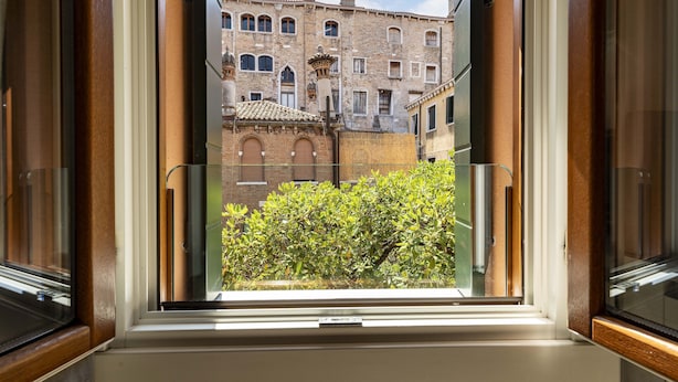 Una ventana con vista a un edificio histórico de múltiples ventanales y tejado de tejas.