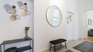 Ein modernes Wohnzimmer mit einer schwarzen Bank, einem Konsolentisch mit dekorativen Tellern, einem großen Spiegel und einem gemusterten Teppich.