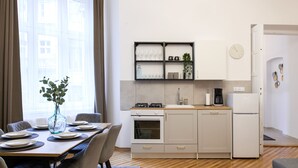 Eine moderne Küche mit weißen Schränken, einem eingebauten Backofen und einer Kaffeemaschine. Ein Esstisch ist gedeckt mit Geschirr und eine Vase mit Blumen steht darauf.