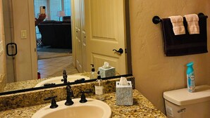Un baño con lavamanos, espejo, toallero y retrete.