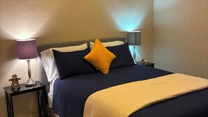 Un dormitorio con una cama, dos lámparas de noche, un ventilador de techo y una pequeña mesa con lámpara.