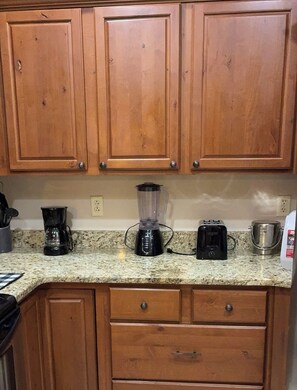Una cocina con armarios de madera, encimera de granito, licuadora, cafetera y hervidor.