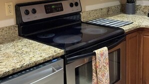 A kitchen with wooden cabinets, a stainless steel microwave, a stove with a digital display, and a granite countertop.