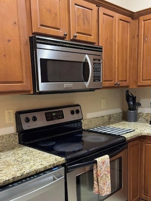 A kitchen with wooden cabinets, a stainless steel microwave, a stove with a digital display, and a granite countertop.