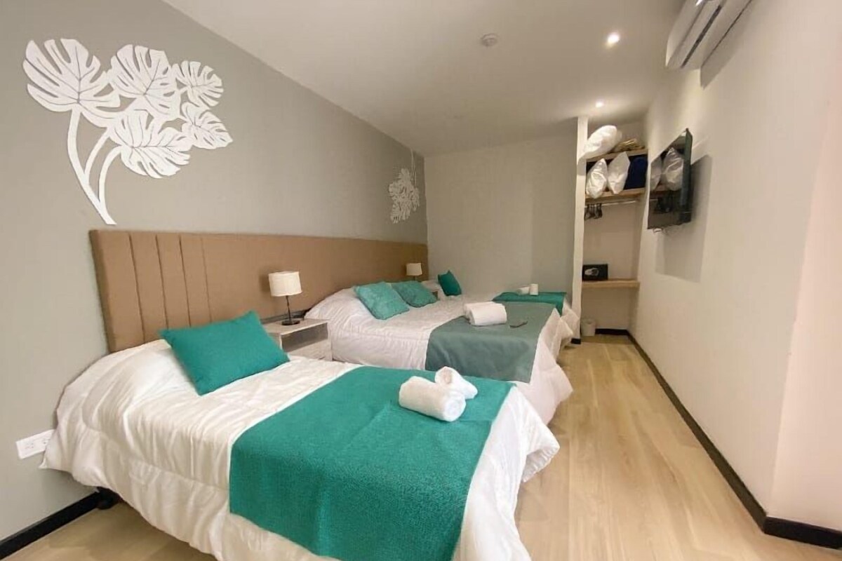 Habitación de hotel con dos camas, cabecero de madera, decoración en la pared, televisor y estante con almohadas.