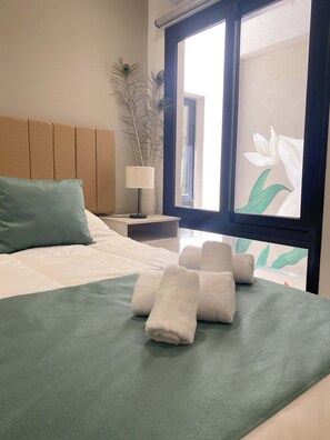 A neatly made bed with a green bedspread, a teal pillow, and rolled white towels.