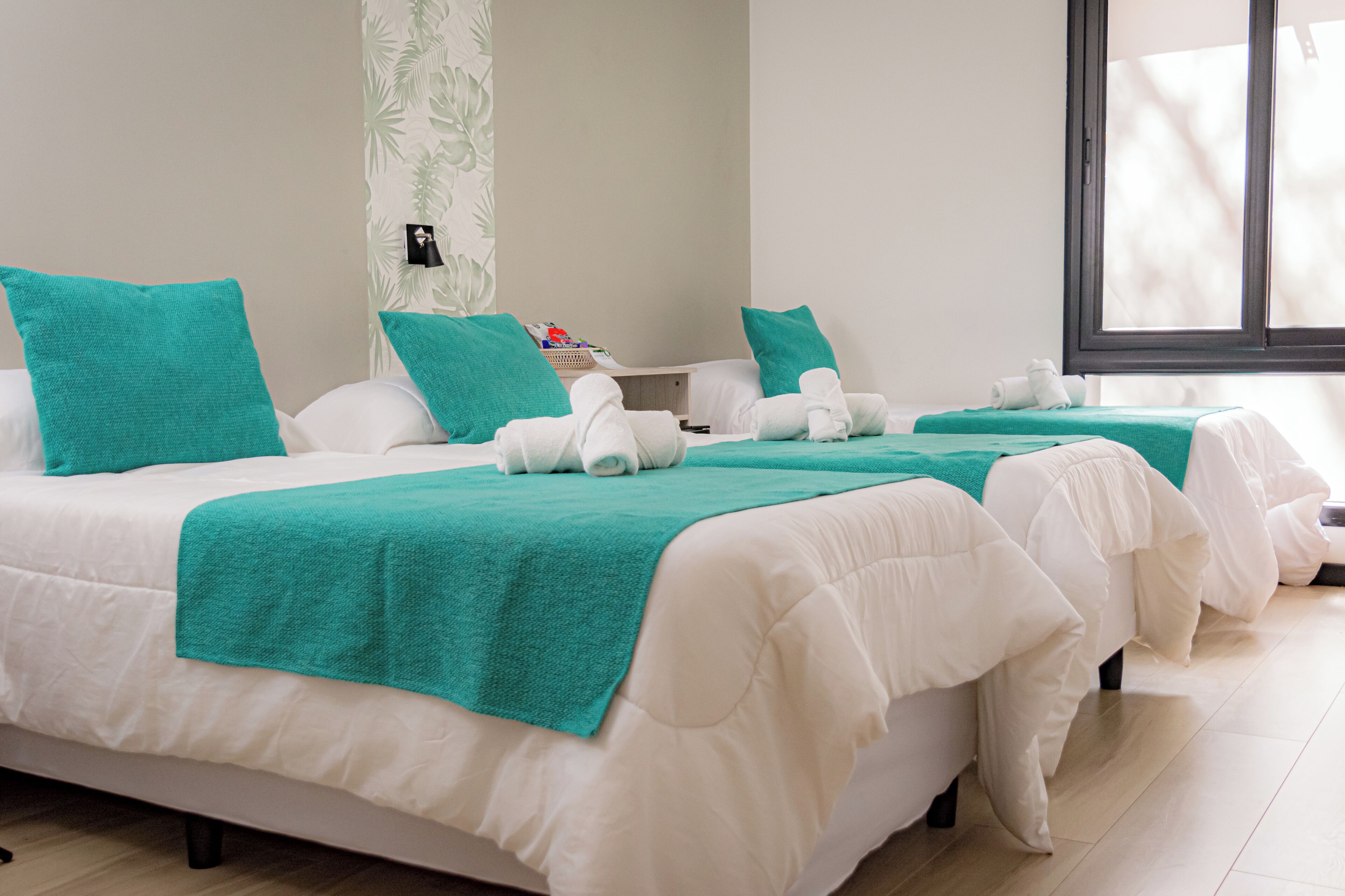 A hotel room with two beds, each with white bedding and teal pillows, and a teal throw blanket.
