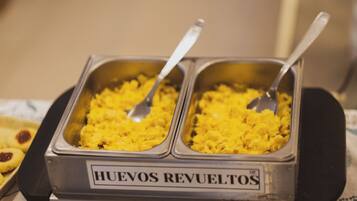 Buffet com dois recipientes rotulados "HUEVOS REVUELTOS" e uma colher em cada um.