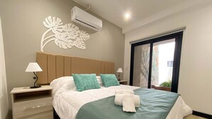 A neatly arranged bedroom with a bed, bedside tables, a lamp, an air conditioner, and a window with a view. - Hotel Caseros Salta (Salta)