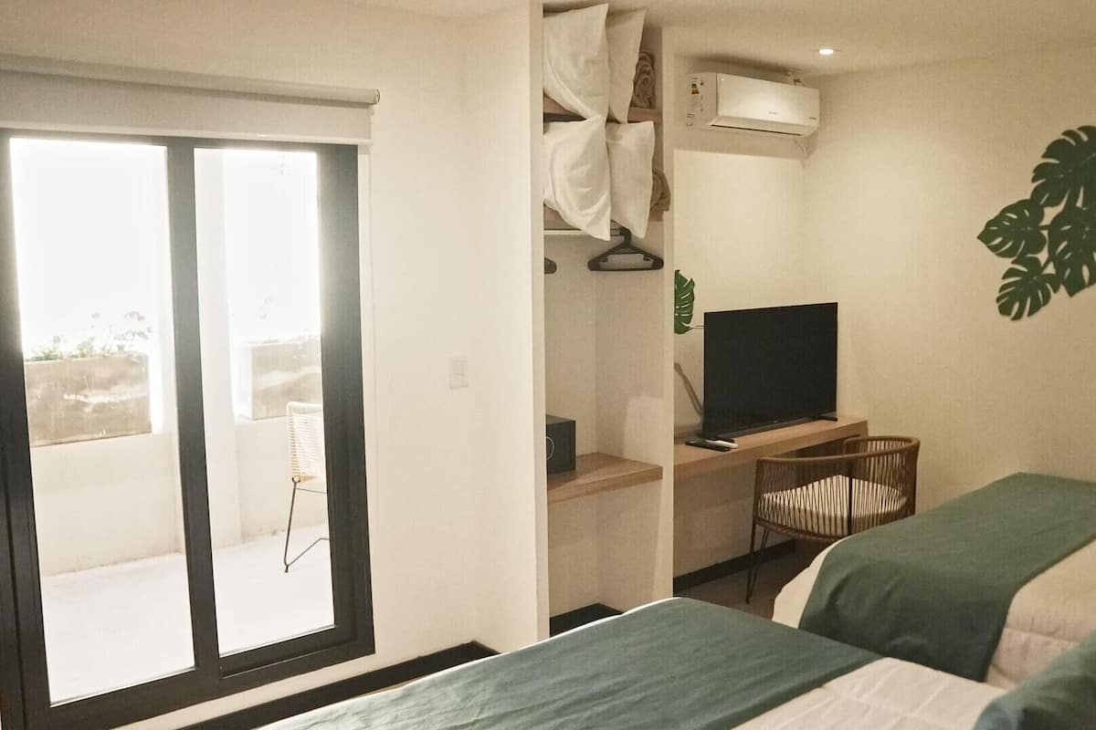 A hotel room with two beds, a TV, a desk, and a large window.