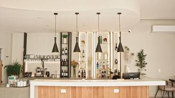 Un bar moderno con mostrador de madera, lámparas colgantes negras y estanterías llenas de botellas y vasos.