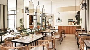 A modern restaurant interior with high ceilings, natural light, and a mix of wooden and wicker furniture. - Hotel Caseros Salta (Salta)