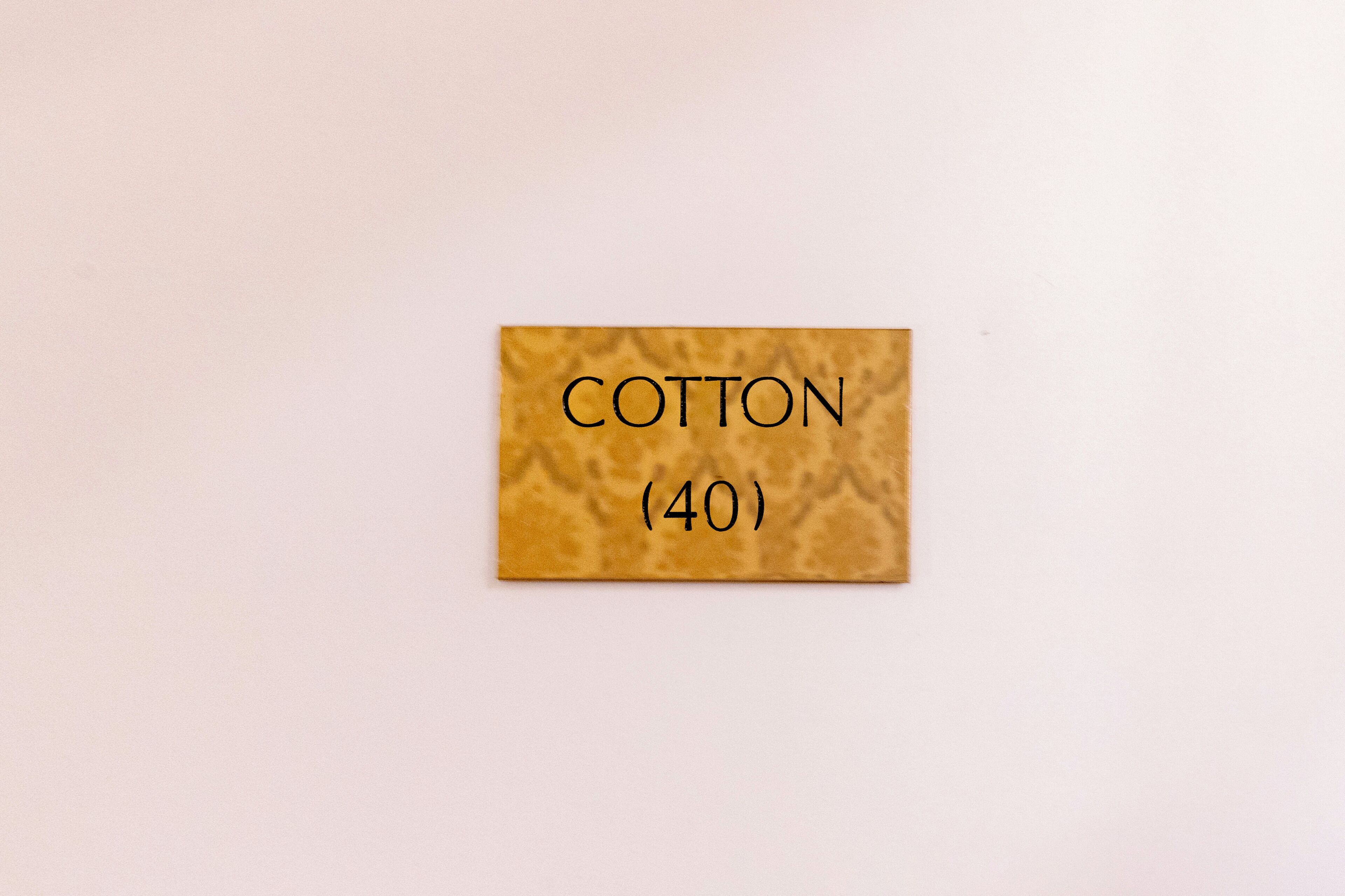 Un pequeño letrero rectangular con la palabra 'COTTON' y el número (40) sobre un fondo liso.