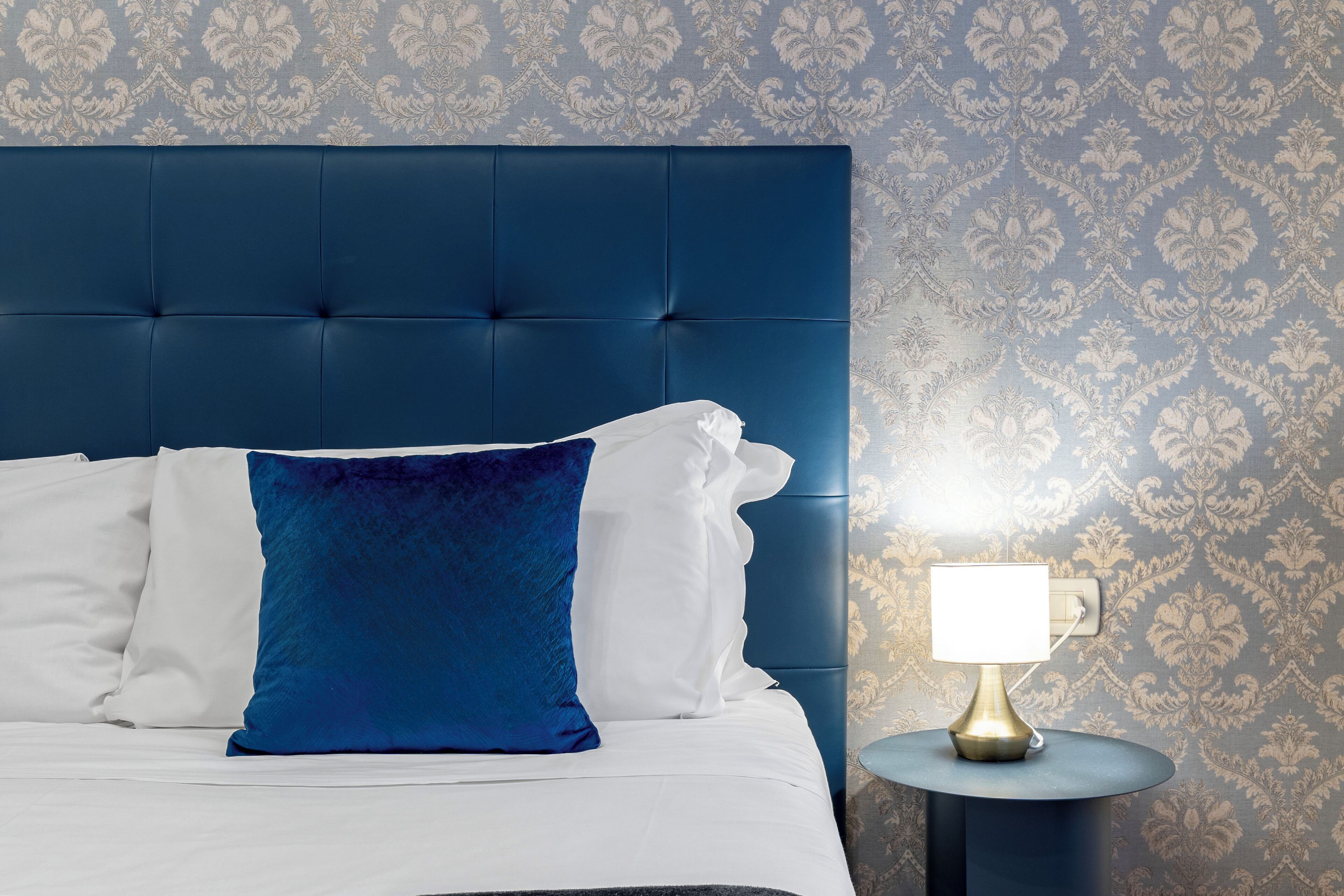 A bed with a blue headboard, white and blue pillows, and a bedside table with a lamp.