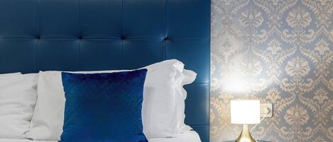 A bed with a blue headboard, white and blue pillows, and a bedside table with a lamp.