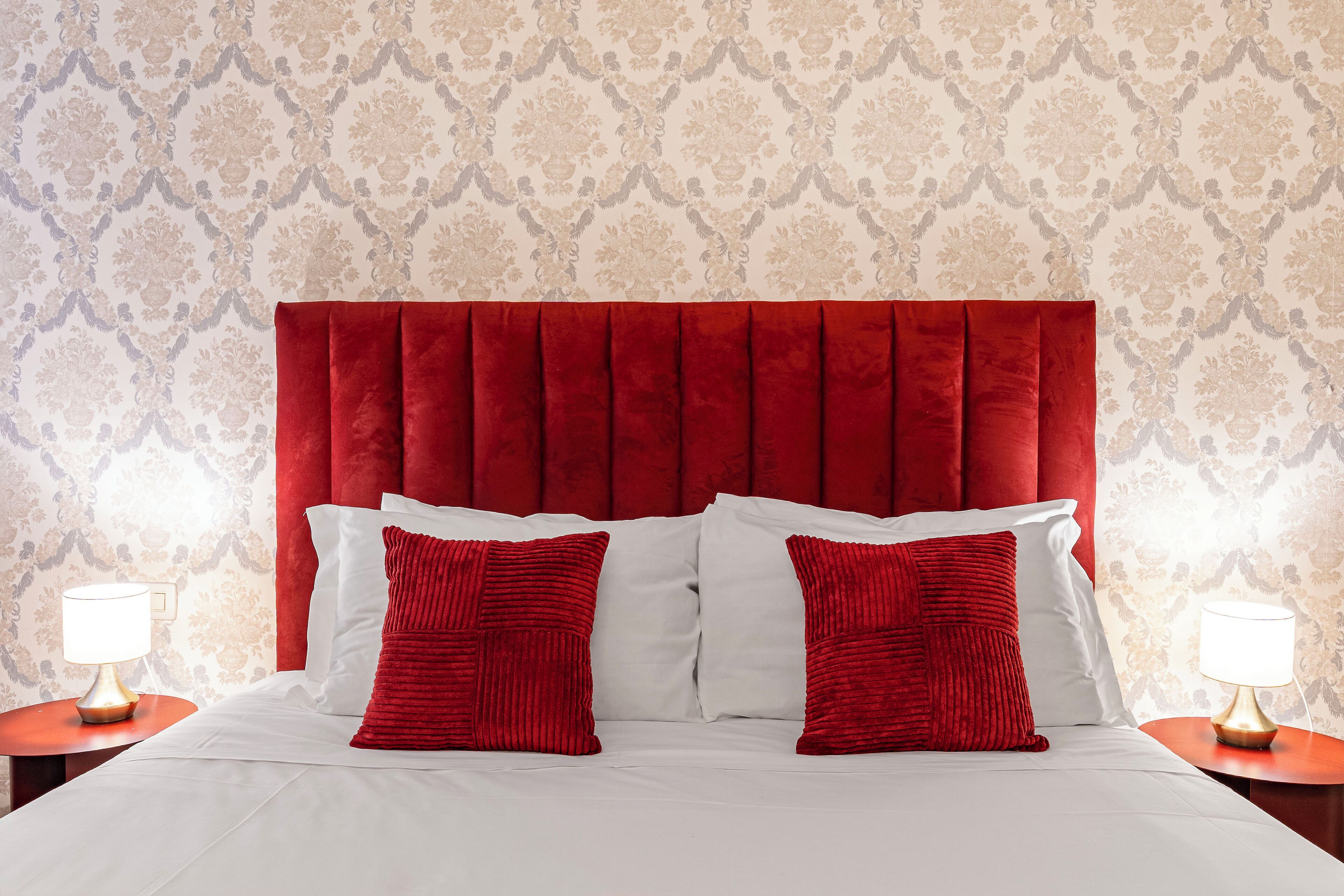 A bed with a red upholstered headboard, white bedding, and two red pillows. There are two bedside tables with lamps.