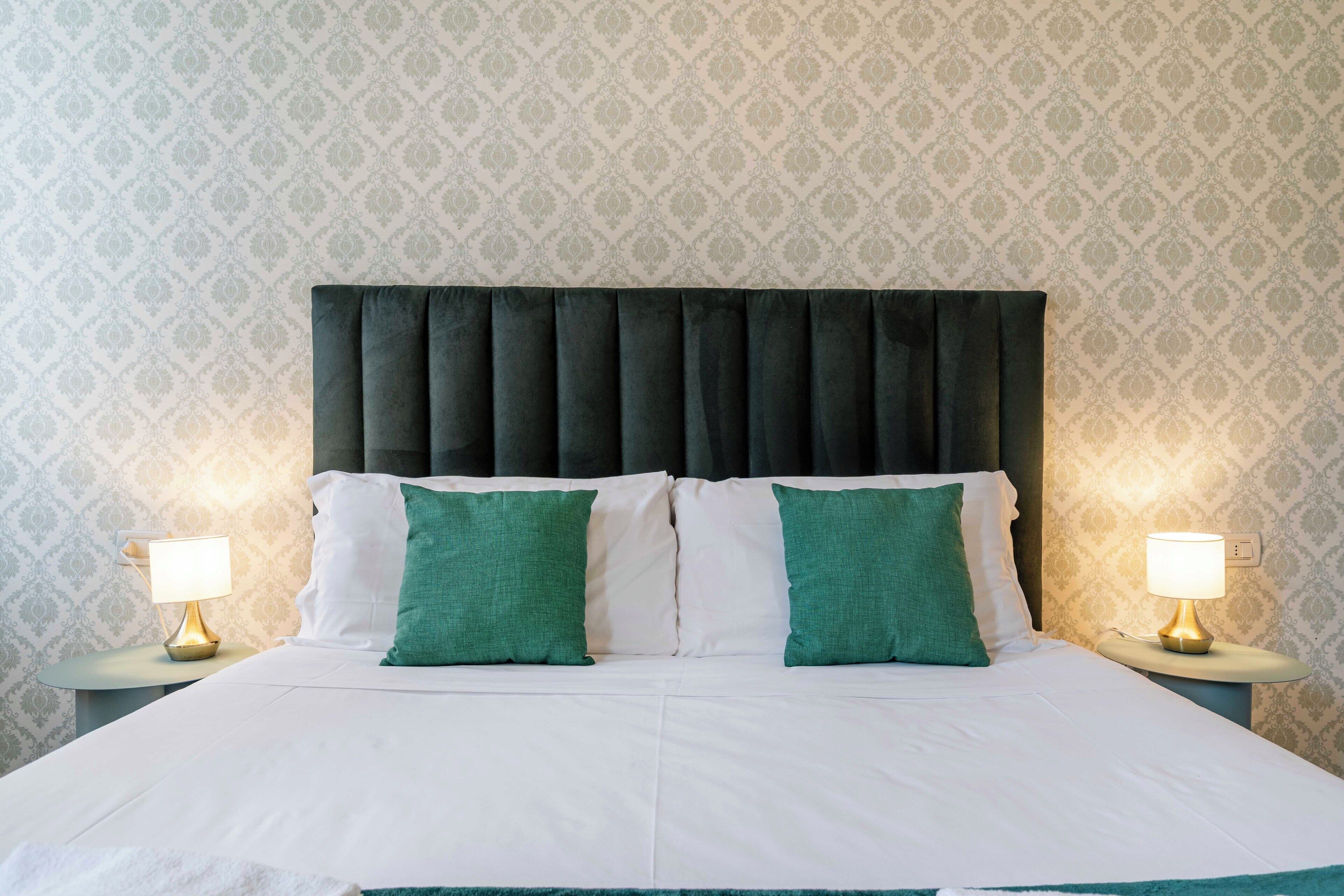 A bed with a dark headboard, white bedding, and two green pillows. There are two bedside tables with lamps.