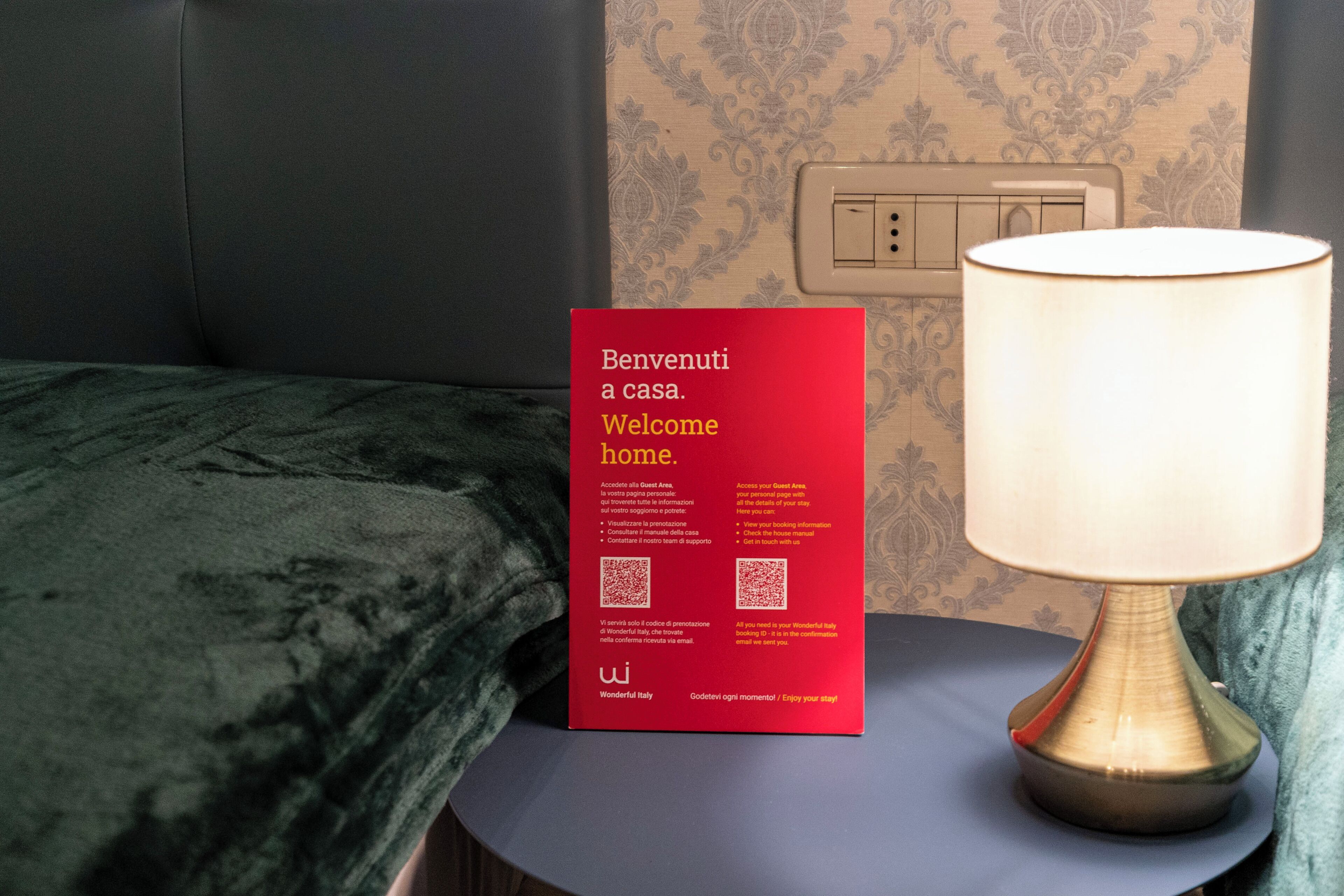 A red welcome sign with QR codes and text, a bedside lamp, and a patterned wall.