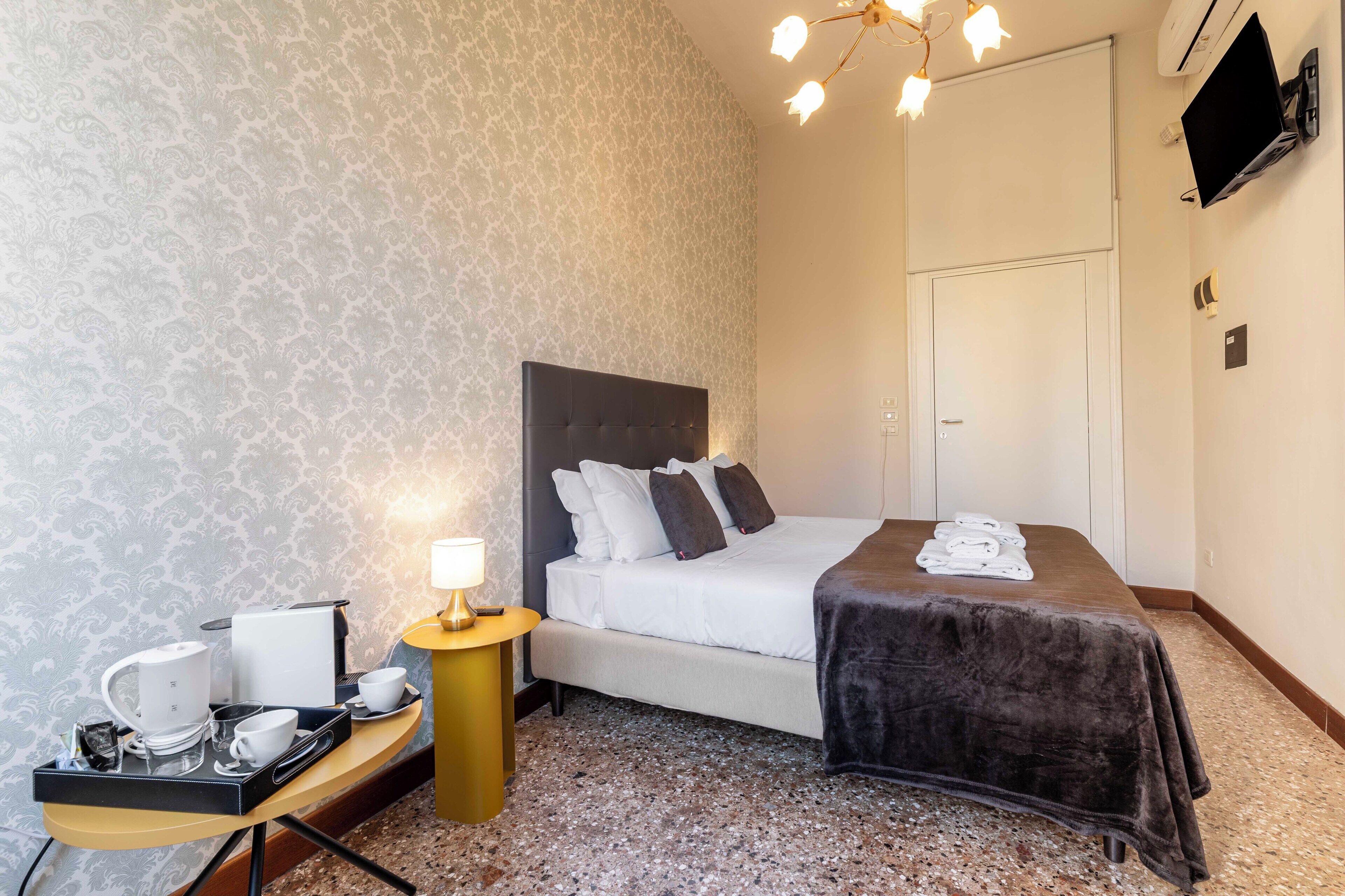 Hotellihuone, jossa on sänky, yöpöytä, lamppu ja seinälle asennettu televisio.