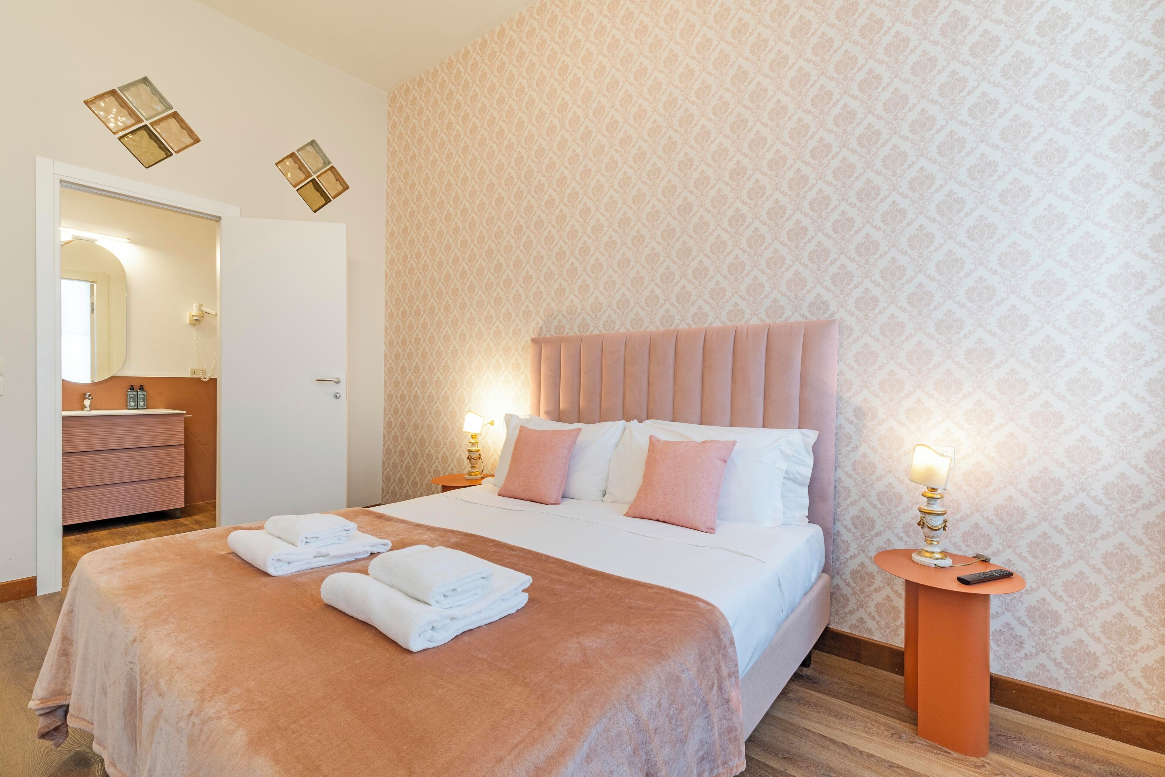 A hotel room with a large bed, a bedside table, a nightstand, a mirror, and a patterned wall.