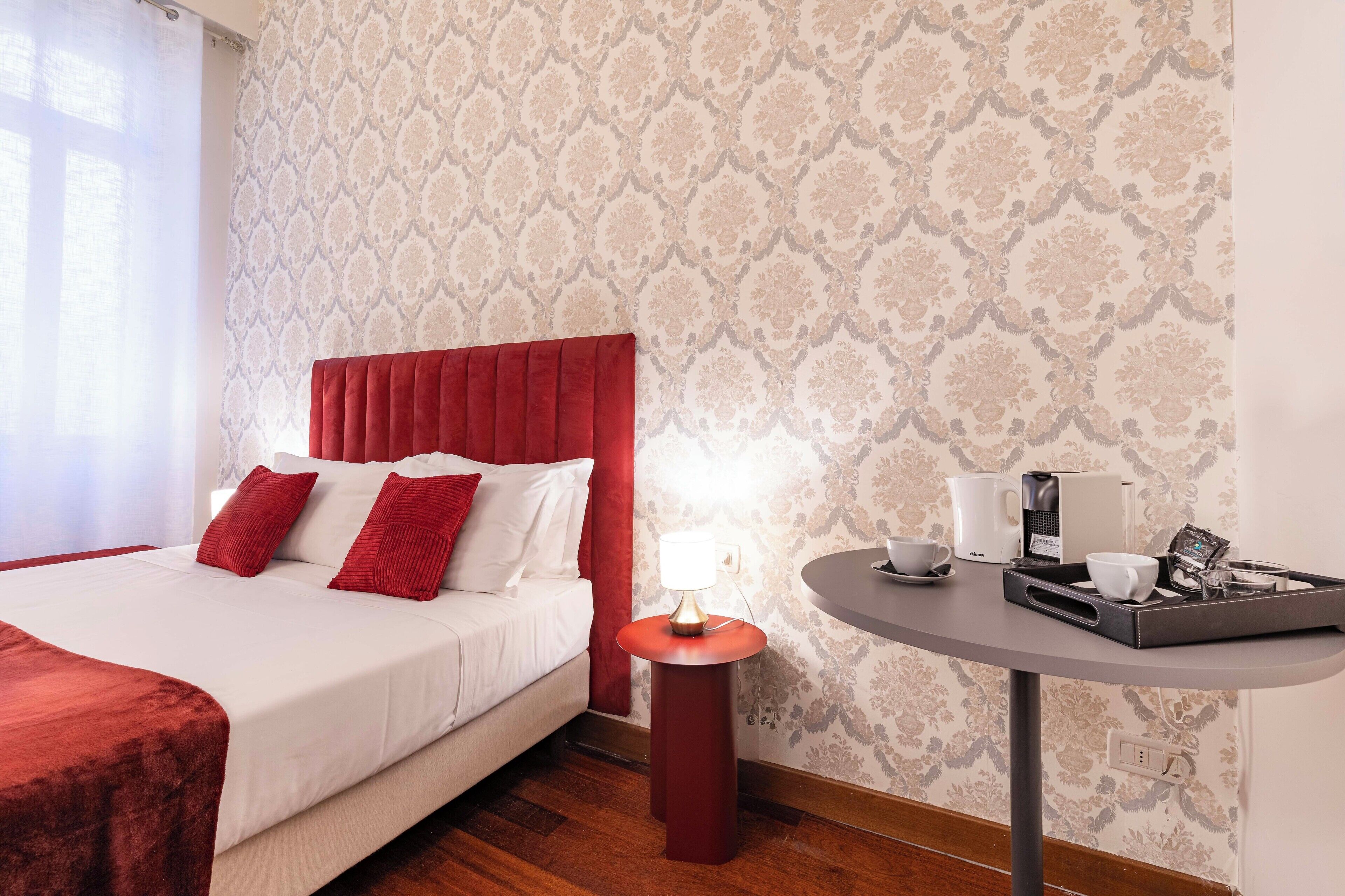 A hotel room with a bed, a bedside table with a lamp, and a tray with cups and a coffee maker.