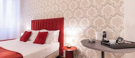 A hotel room with a bed, a bedside table with a lamp, and a tray with cups and a coffee maker.