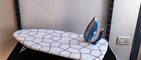 Ein kompakter Bügelplatz mit einem Bügelbrett mit geometrischem Muster, einem blauen Bügeleisen und einer Steckdose an der Wand.