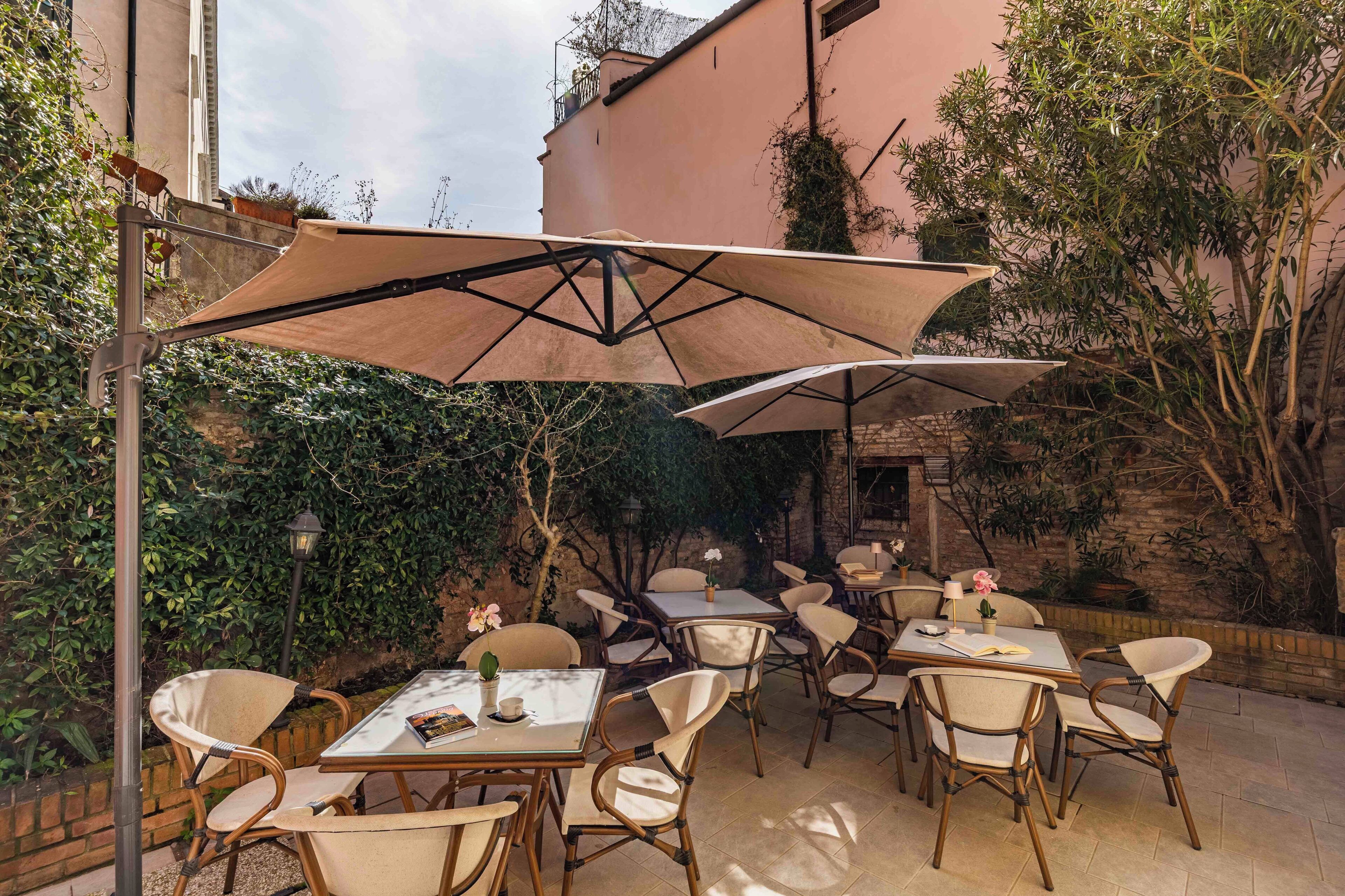 An outdoor patio with tables and chairs, surrounded by greenery and a building.