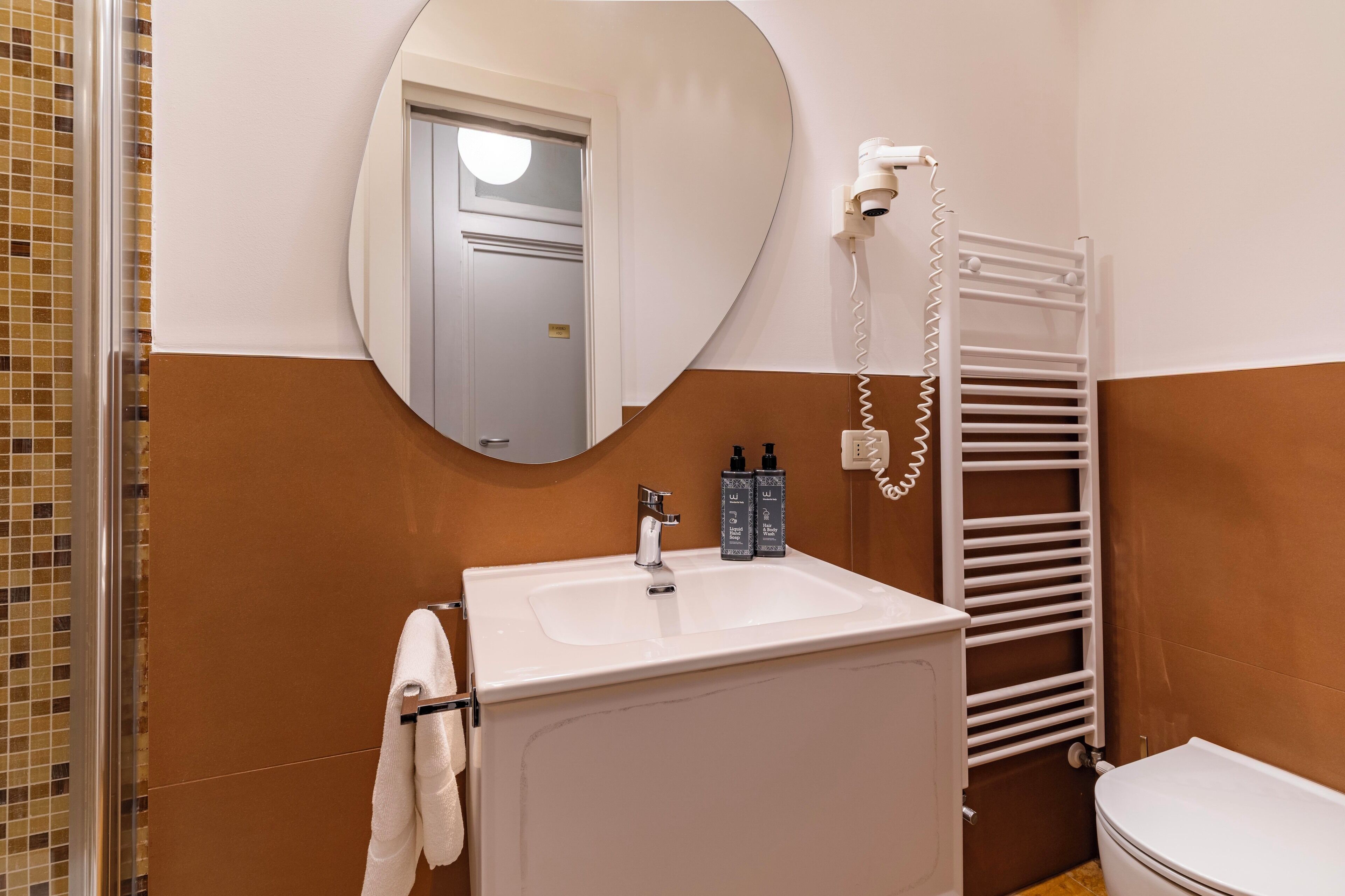 Une salle de bain avec un lavabo blanc, un miroir, un porte-serviettes, des toilettes et une serviette suspendue au porte-serviettes.