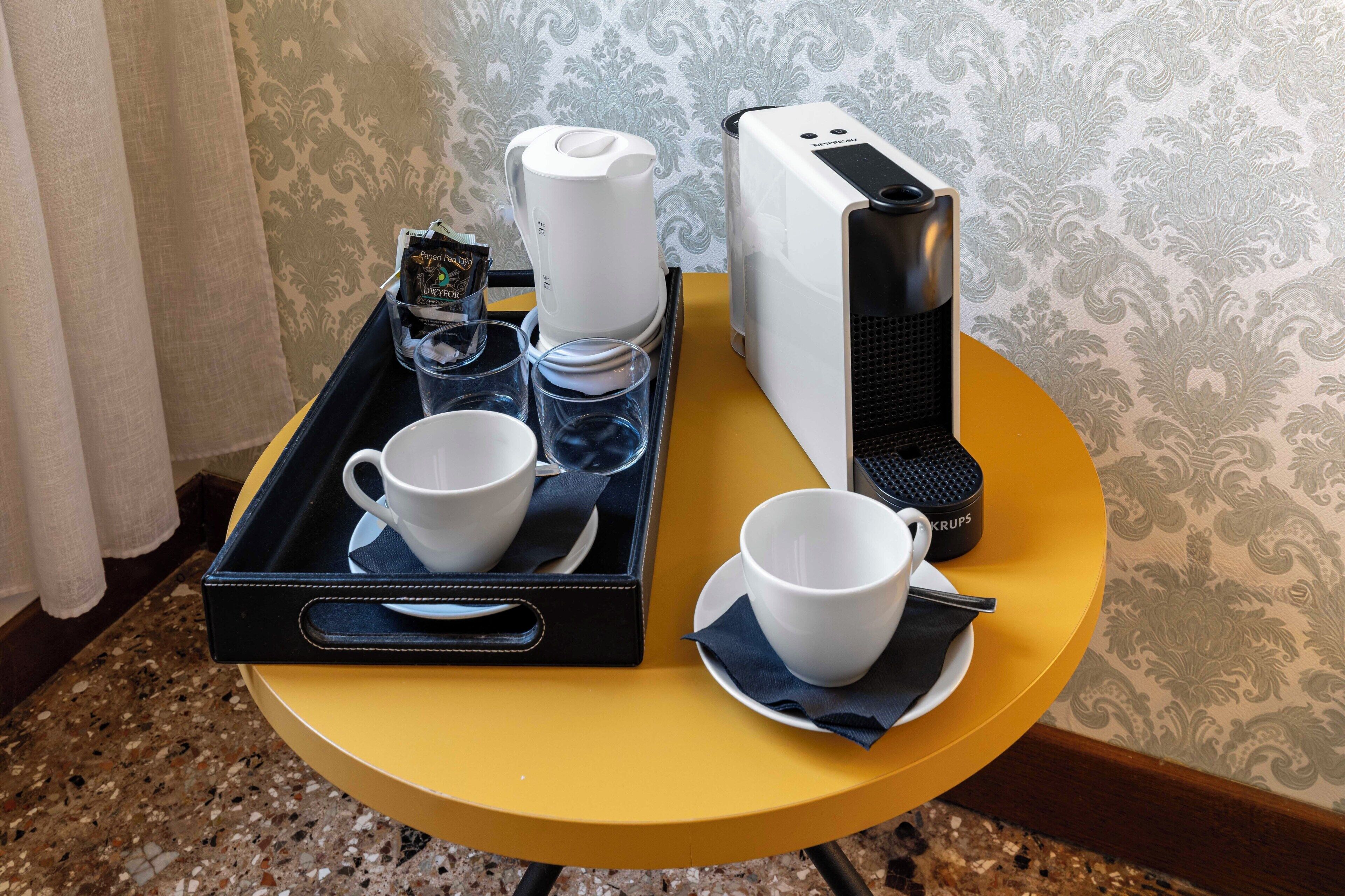 Ein Tablett mit zwei Tassen, einer Kaffeemaschine und einer Bürste auf einem gelben Tisch.