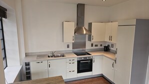 A modern kitchen with white cabinets, stainless steel appliances, and a wooden table. - Travaal.com - FREE-WIFI-NETFLIX-PARKING - 2 Bedroom Apartment - Farnborough (Farnborough)