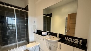 A modern bathroom with a shower, toilet, sink, and a large mirror. - Travaal.com - FREE-WIFI-NETFLIX-PARKING - 2 Bedroom Apartment - Farnborough (Farnborough)