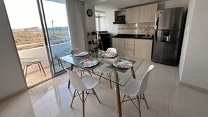 A modern kitchen with a dining area, featuring a large window, stainless steel appliances, and a balcony with a view.