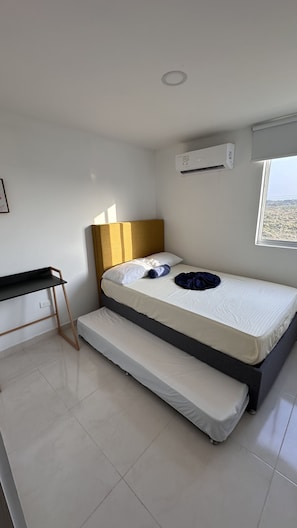 A bedroom with a bed, a desk, and an air conditioning unit.