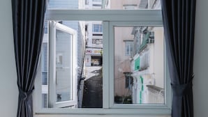 A bedroom with a bed, a window with curtains, and a view of buildings outside. - 42 Da Lat Hotel (Xuan Huong - Da Lat)