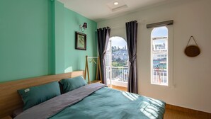 A bedroom with a bed, a window with curtains, a small table, and a wall-mounted lamp. - 42 Da Lat Hotel (Xuan Huong - Da Lat)