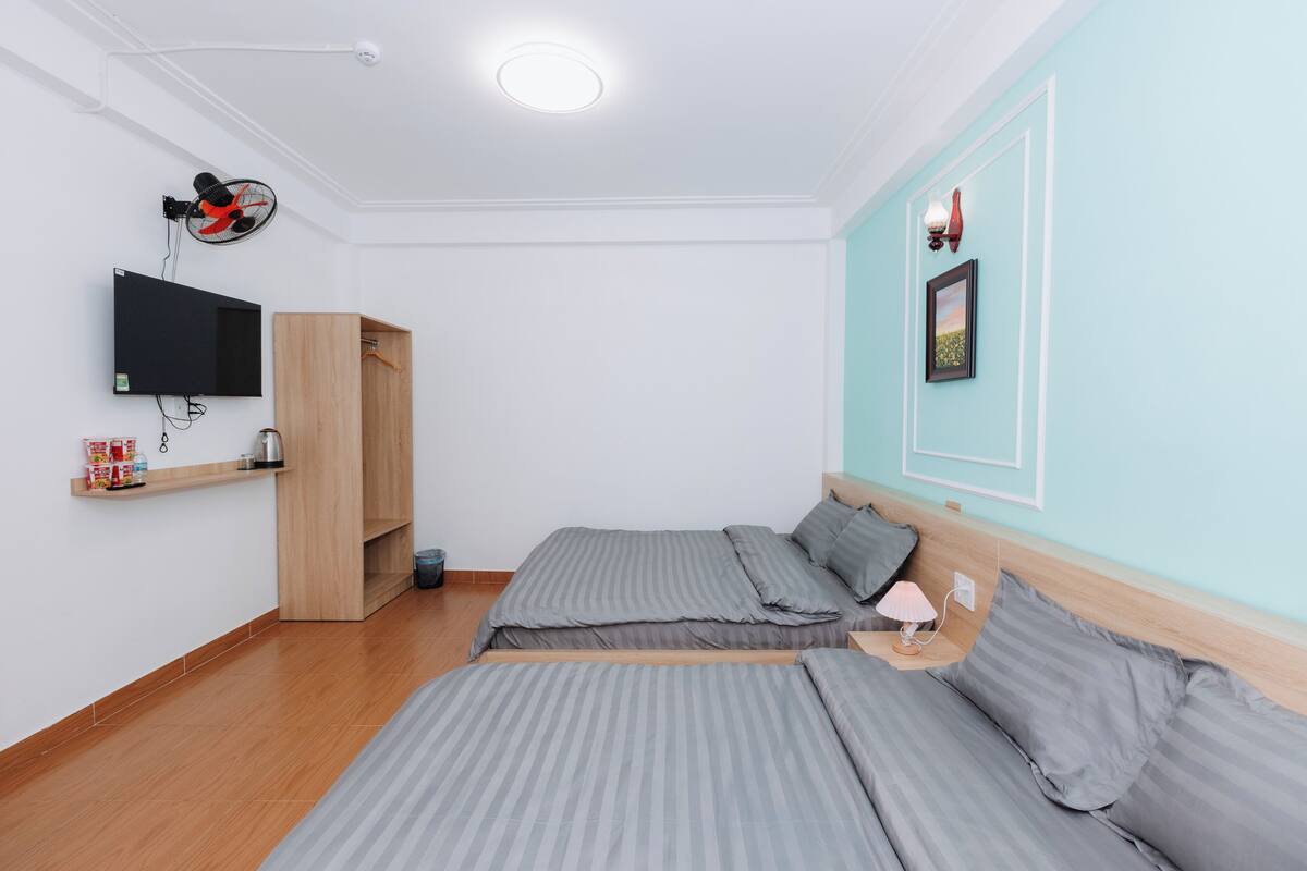 A bedroom with two beds, a TV mounted on the wall, a wardrobe, and a small shelf with items.