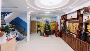 A hotel lobby with a Christmas tree, wooden shelves with decorations, a staircase, and a mural on the wall. - 42 Da Lat Hotel (Xuan Huong - Da Lat)